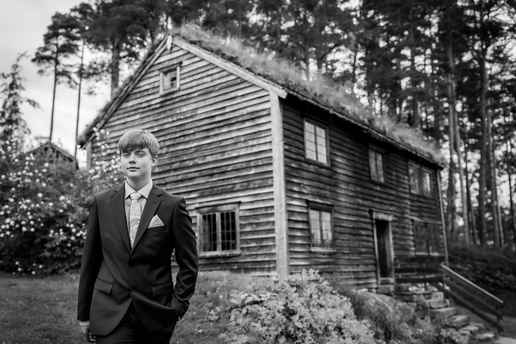Konfirmant utenfor gammelt tømmerhus, fotografert av Marte Bjørgum