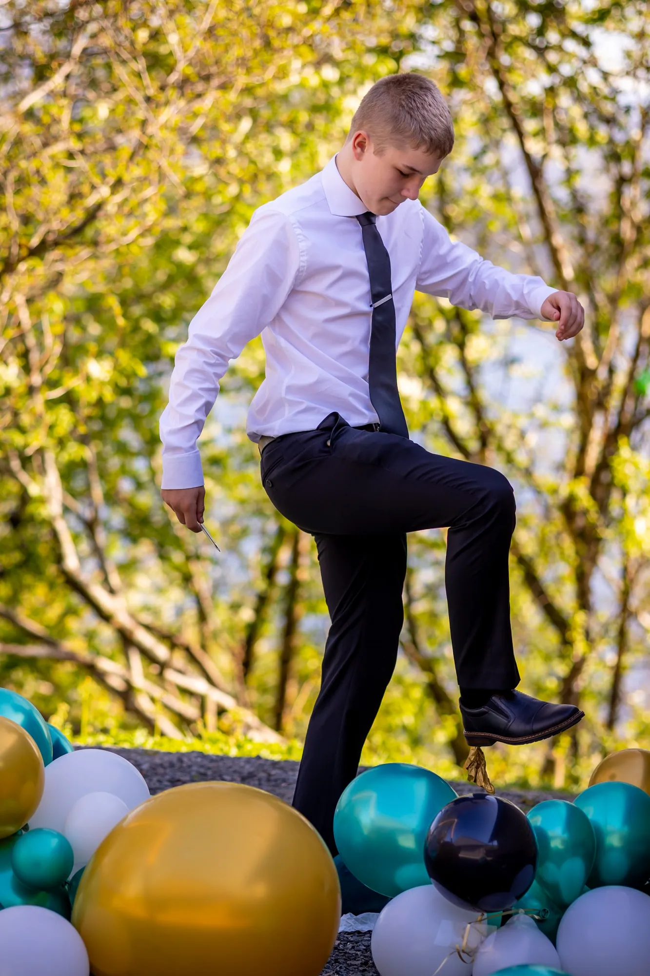 Konfirmant i dress og slips midt i et sprett, ballonger rundt