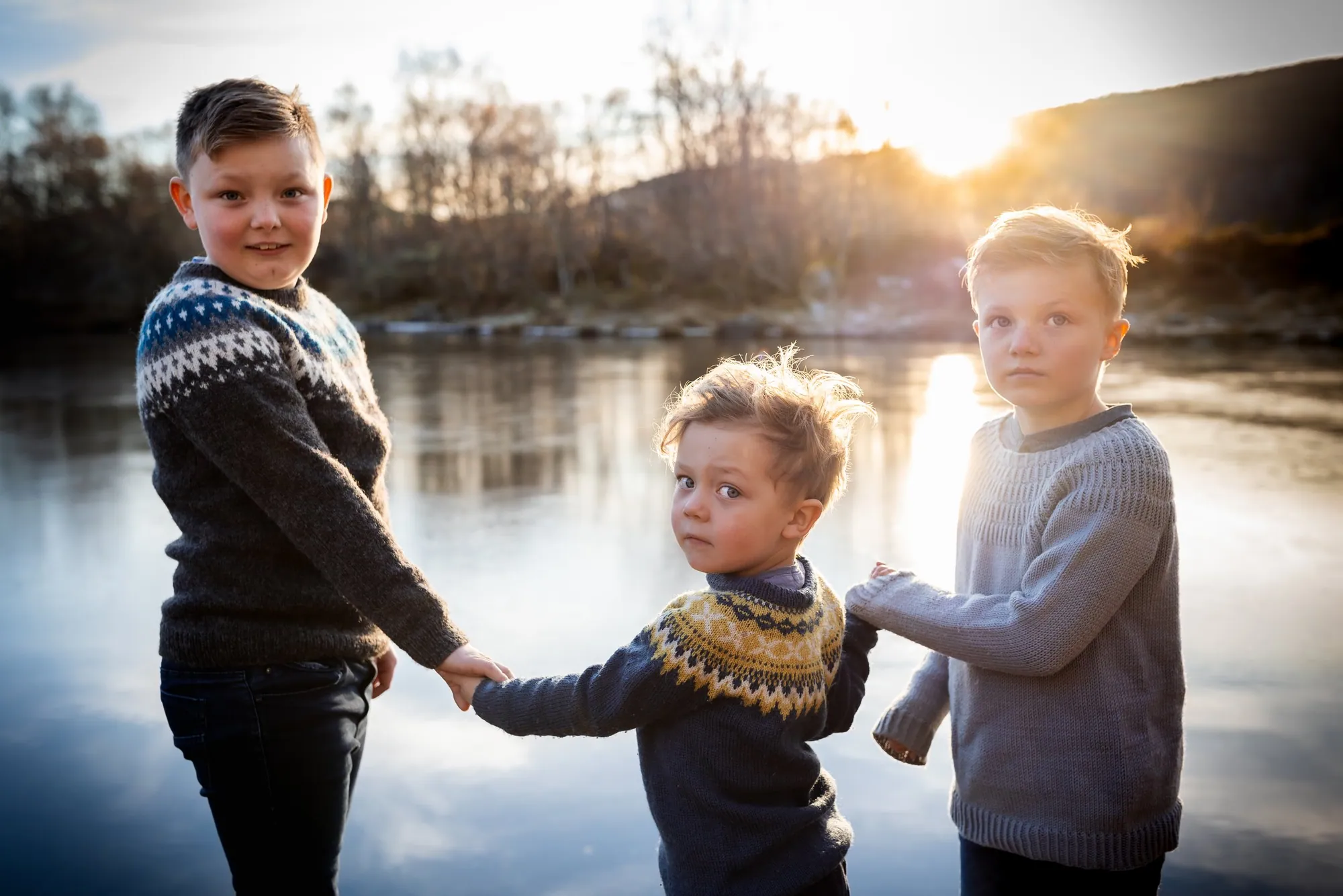 Tre brødre som går hånd i hånd mot vannet i gyllent kveldslys